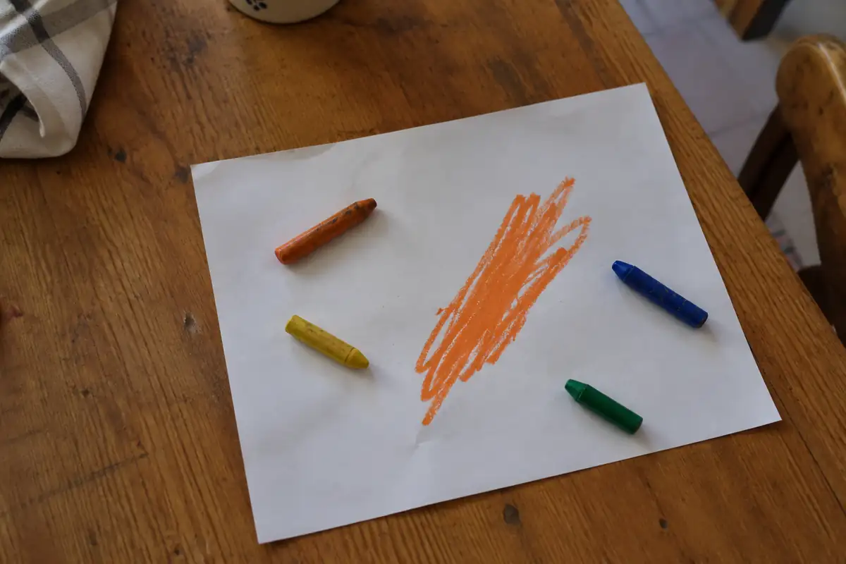 Crayons de cire posés autour d'un trait orange épais sur une feuille blanche