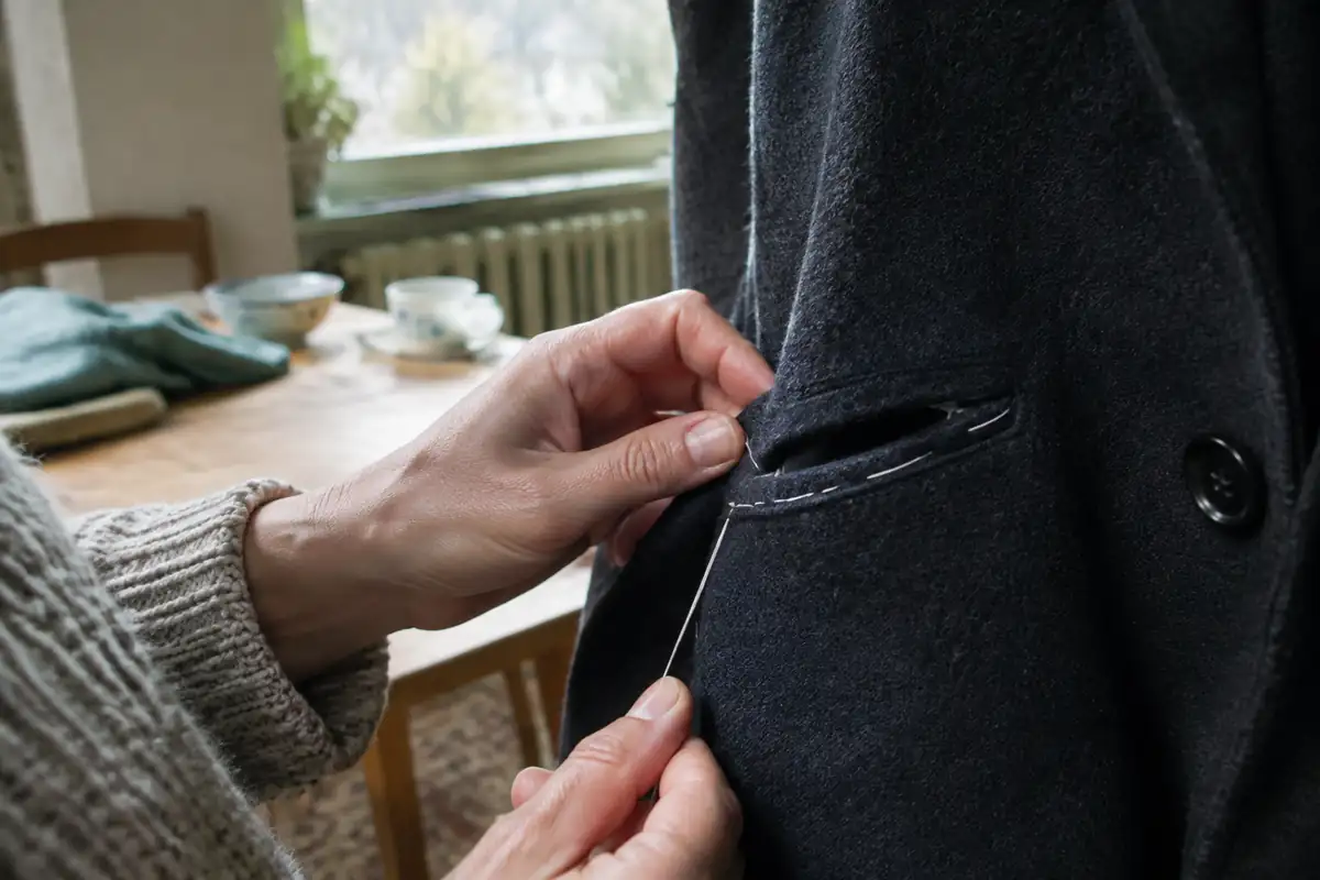 Doigts tirant un fil de bâti blanc hors de la poche d'un manteau en laine