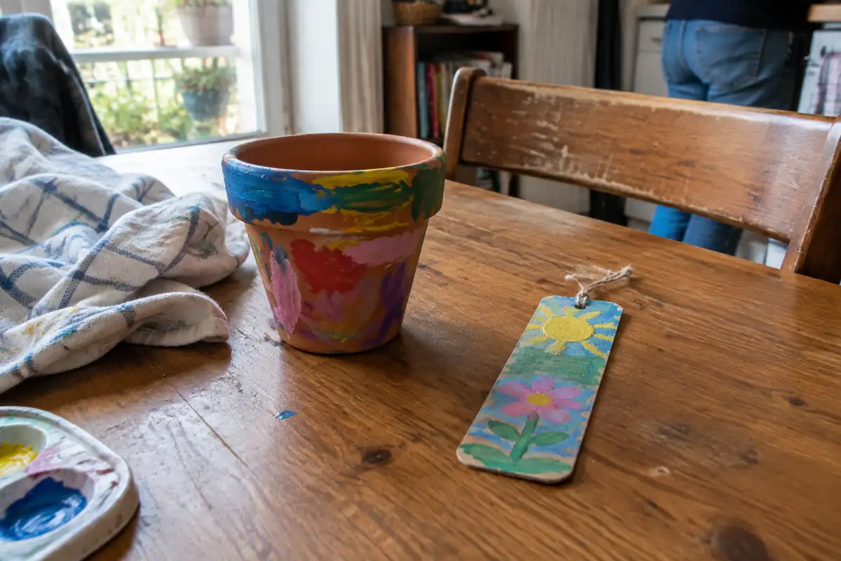 Un pot en terre cuite peint de couleurs vives et un marque-page décoré, posés sur une table pour sécher